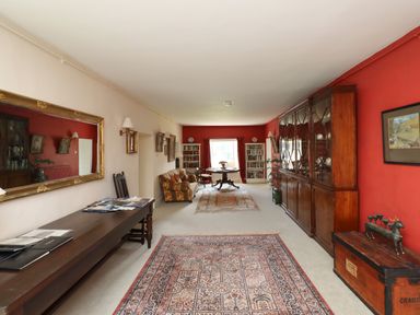 A long living room with a patterned rug on the floor a wooden table with chairs a sofa and a large wooden cabinet against a red wall at Craster Tower Penthouse in Craster