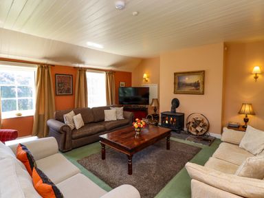 A living room with three sofas a wooden coffee table a wood burning stove and a television at Craster Tower Penthouse in Craster