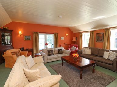 A living room with multiple sofas a wooden coffee table with flowers and orange walls at Craster Tower Penthouse in Craster
