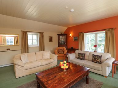 A living room with two sofas an armchair a wooden coffee table with flowers and windows with curtains at Craster Tower Penthouse in Craster