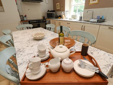 A kitchen with a marble patterned table and blue chairs with a tray holding a teapot cups plates and utensils at Craster Tower Penthouse in Craster