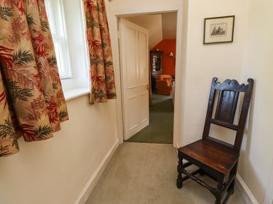 A narrow hallway with patterned curtains on the window and a wooden chair against the wall at Craster Tower Penthouse in Craster