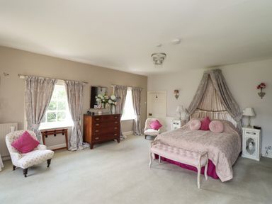 A bedroom with a bed canopy two armchairs wooden dresser and two windows at Craster Tower Penthouse in Craster