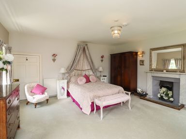 A bedroom with a bed draped with fabric a wooden wardrobe a fireplace and an armchair at Craster Tower Penthouse in Craster