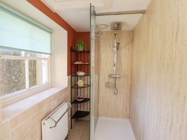 A shower with glass partition and black corner shelf under a window at Craster Tower Penthouse in Craster