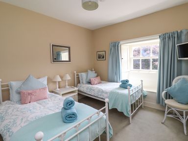 A bedroom with two single beds bedside table with lamps a window with curtains and a chair with cushions at Craster Tower Penthouse in Craster