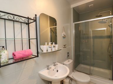 A bathroom with a sink and toilet beside a glass shower enclosure and a wall shelf with toiletries at Craster Tower Penthouse in Craster