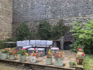 An outdoor patio with a corner sofa and table surrounded by potted plants and a stone wall at Craster Tower Penthouse in Craster