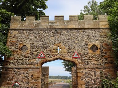 A stone archway with two triangular height restriction signs on a rural road surrounded by trees at Craster Tower Penthouse in Craster