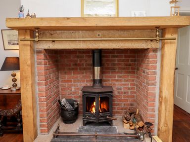 A brick fireplace with a black wood stove and firewood at No2 Budle Bay Cottage in Bamburgh