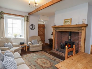 A living room with a fireplace two armchairs a sofa a wooden door and a dining table at No2 Budle Bay Cottage Bamburgh