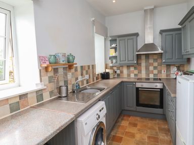 A kitchen with grey cabinetry a washing machine an oven a fridge and a tiled backsplash at No2 Budle Bay Cottage in Bamburgh