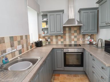 A kitchen with grey cabinets a stainless steel oven stovetop and hood a tiled backsplash and countertop at No2 Budle Bay Cottage Bamburgh