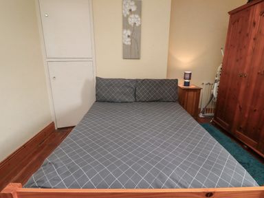 A bedroom with a double bed with grey checkered bedding a wooden wardrobe a wooden nightstand with a lamp and wooden flooring at No2 Budle Bay Cottage in Bamburgh