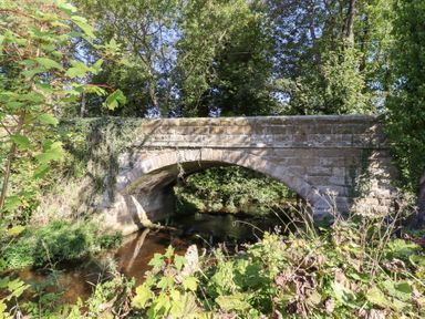 A stone bridge over a stream surrounded by trees and vegetation at Pippin in Lucker