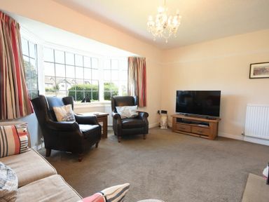 A living room with two black armchairs a sofa a television on a wooden stand and large bay windows at Inveray in Seahouses