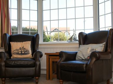 Two leather armchairs with decorative pillows next to a wooden side table in front of large windows at Inveray in Seahouses