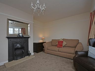 A living room with a brown sofa a black fireplace a mirror and a chandelier at Inveray in Seahouses
