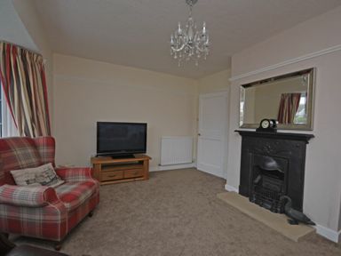 A living room with a fireplace a TV on a wooden stand and a plaid armchair at Inveray in Seahouses