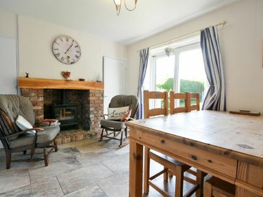 A dining area with wooden table and chairs near a fireplace and sliding glass doors with striped curtains at Inveray in Seahouses
