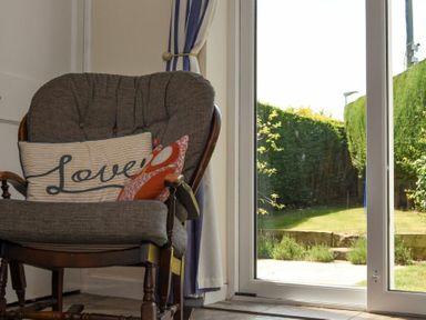 A cushioned wooden armchair with pillows next to a glass sliding door showing a garden outside at Inveray in Seahouses