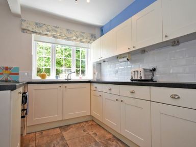 A kitchen with white cabinets black countertops a window with floral valance a toaster and a tiled floor at Inveray in Seahouses