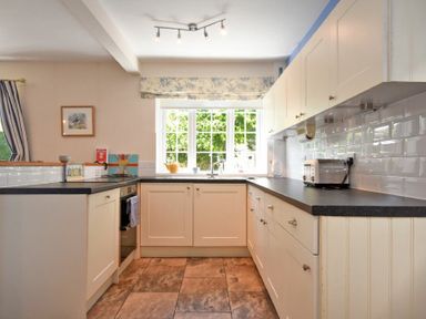 A kitchen with white cabinets black countertops a window above the sink and a toaster on the counter at Inveray in Seahouses