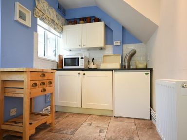 A small kitchen with a wooden side table microwave under cabinet fridge and radiator at Inveray in Seahouses