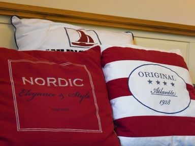Close up of three decorative pillows including red and white striped cushions with text on a bed at Inveray in Seahouses