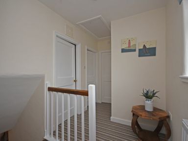 A hallway with striped carpet a small wooden table with a plant and two paintings on the wall at Inveray in Seahouses