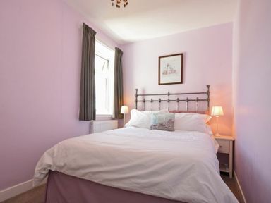 A bedroom with a bed white bedding bedside tables with lamps and a window with dark curtains at Inveray in Seahouses