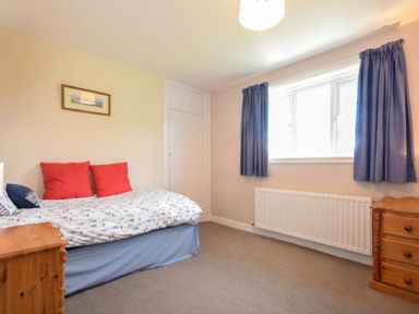 A bedroom with a bed with red pillows a framed picture on the wall a window with blue curtains and wooden bedside tables at Inveray in Seahouses