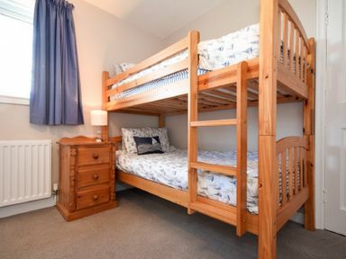 A bedroom with wooden bunk beds a wooden bedside table a lamp and blue curtains at Inveray in Seahouses