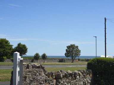 A view of the sea with stone wall bushes trees and a streetlight at Inveray Seahouses