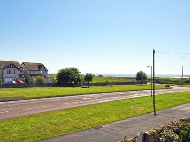 A street with grass verges houses trees and the sea in the background at Inveray in Seahouses