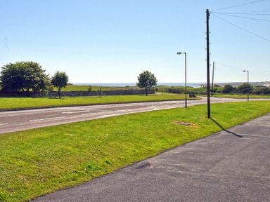 A roadside area with grass, trees, street lamps, and a view of the sea at Inveray in Seahouses