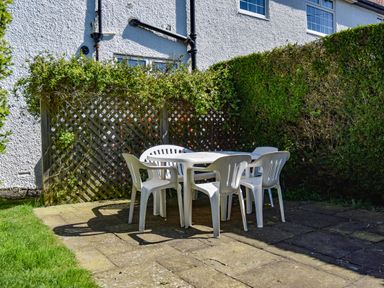 A patio with a white plastic table and chairs next to a hedge and a lattice fence at Inveray in Seahouses