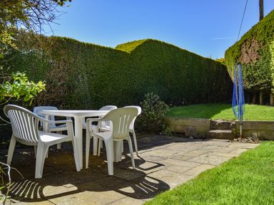 An outdoor patio with a white plastic table and four chairs surrounded by trimmed hedges at Inveray in Seahouses