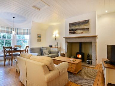 A living room with a wood stove in a stone fireplace a wooden coffee table two sofas a dining table with chairs and a television at Periwinkle in Bamburgh