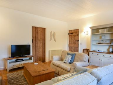 A living room with a television on a stand a wooden coffee table two sofas and a cabinet at Periwinkle in Bamburgh