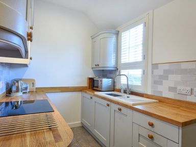 A kitchen with wooden countertops a sink a microwave and cabinets at Periwinkle in Bamburgh