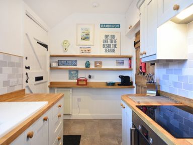 A kitchen with white cabinets wooden countertops shelves with decorations and a stove at Periwinkle in Bamburgh