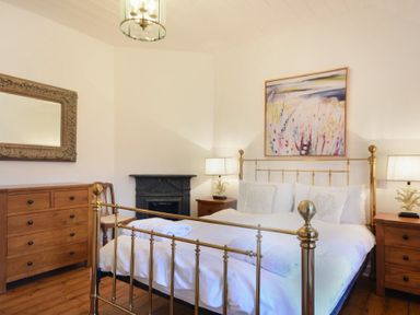 A bedroom with a brass bed frame wooden dressers lamps and a decorative mirror at Periwinkle in Bamburgh