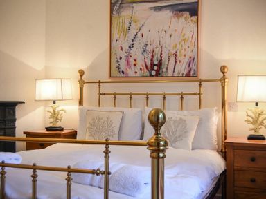 A bedroom with a brass bed frame white bedding bedside tables and lamps at Periwinkle in Bamburgh