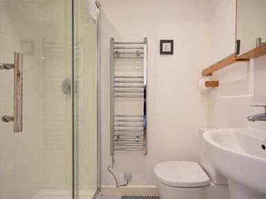 A bathroom with a shower enclosure a toilet a wall-mounted towel radiator and a sink at Periwinkle in Bamburgh