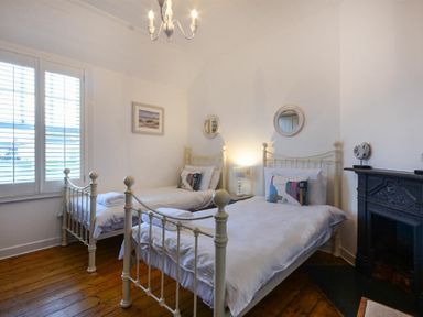 A bedroom with two single beds a window a fireplace and wooden floor at Periwinkle Bamburgh