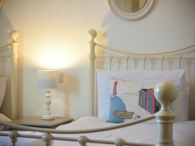 A bedroom with cream metal bed frames a nightstand with a lamp and a decorative pillow at Periwinkle in Bamburgh