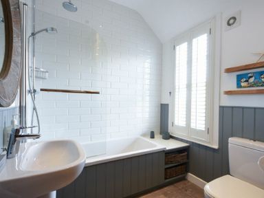 A bathroom with a bathtub shower sink toilet window and shelves at Periwinkle in Bamburgh
