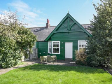 A green house with a white door and windows a garden table with chairs and grass at Periwinkle in Bamburgh