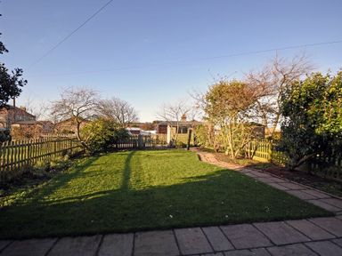 A garden with a grassy lawn stone pathway trees and a wooden fence at Periwinkle in Bamburgh
